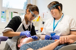 Two clinical staff members providing dental treatment to a patient at a clinic.