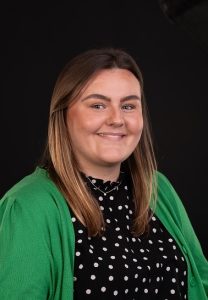Leonora May, Company Secretary at QVH. She has dark hair and is wearing a dark top with white spots on it and a green cardigan.
